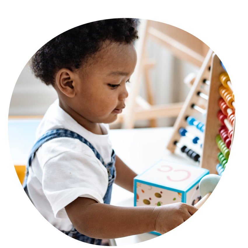 A toddler surrounded by colourful abacuses plays with wooden toys.