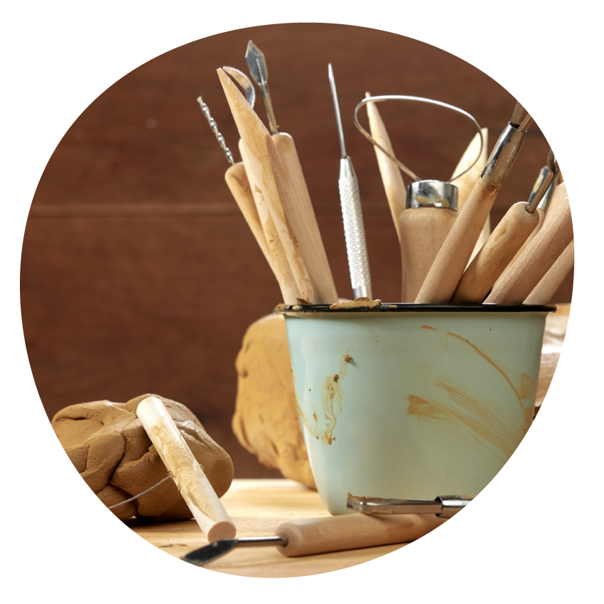 Email Image: A pot holding pottery tools stands on a table next to a lump of clay.