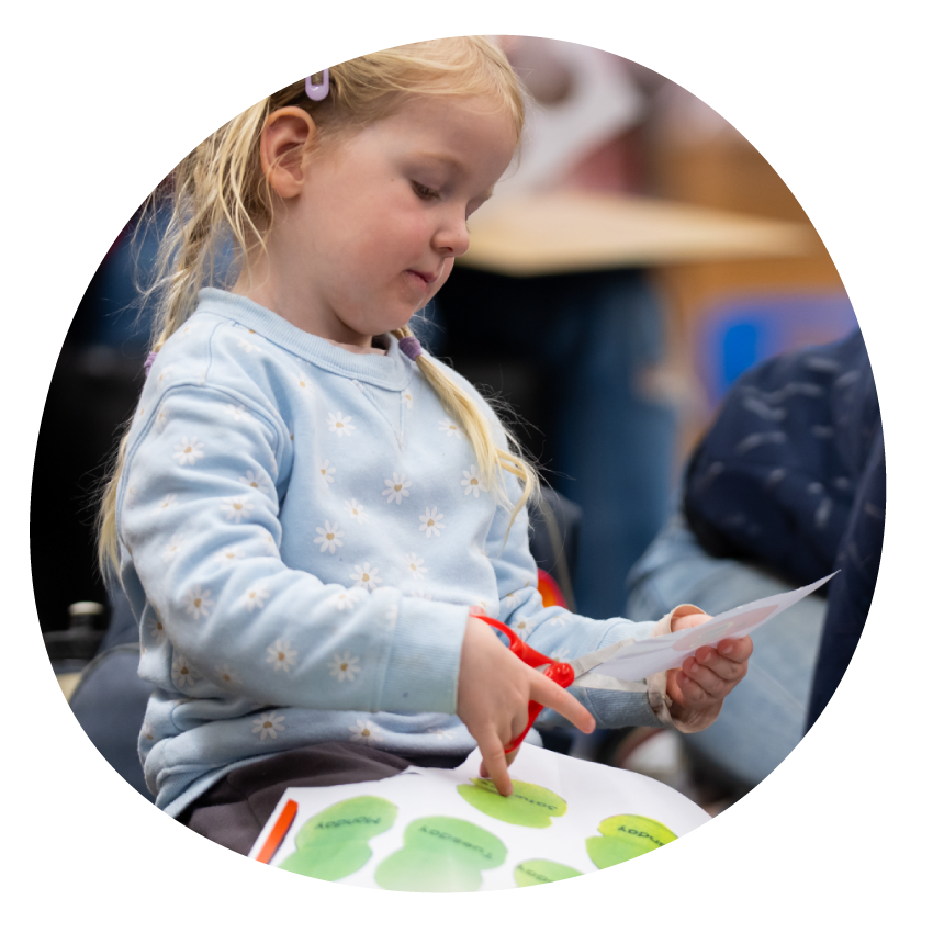 Image: A young child sits on the floor doing paper craft.