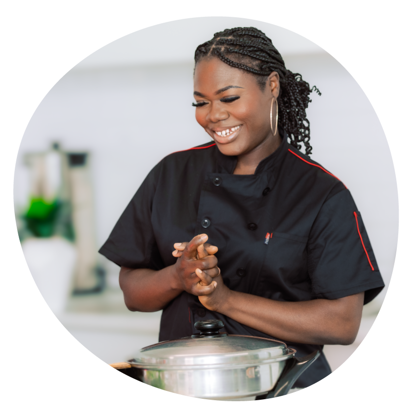 Image: Chef Evette Quoibia in a black chef's jacket stands smiling in a kitchen.