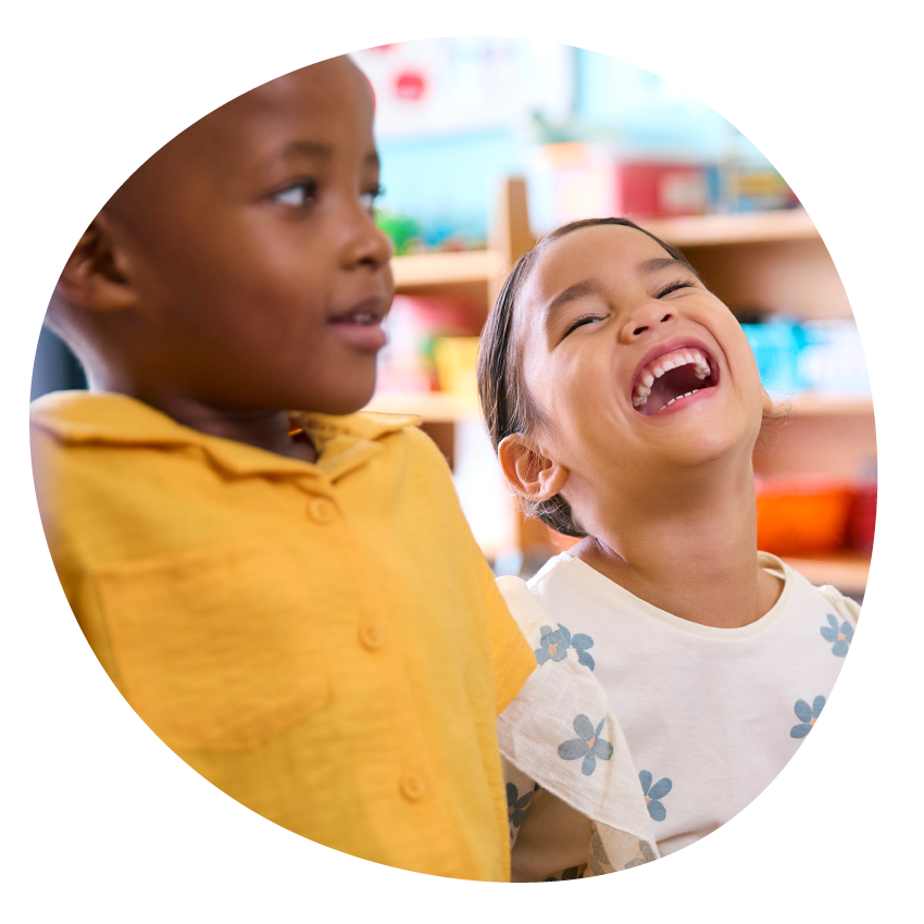Two young children seated together, one with head thrown back in laughter.