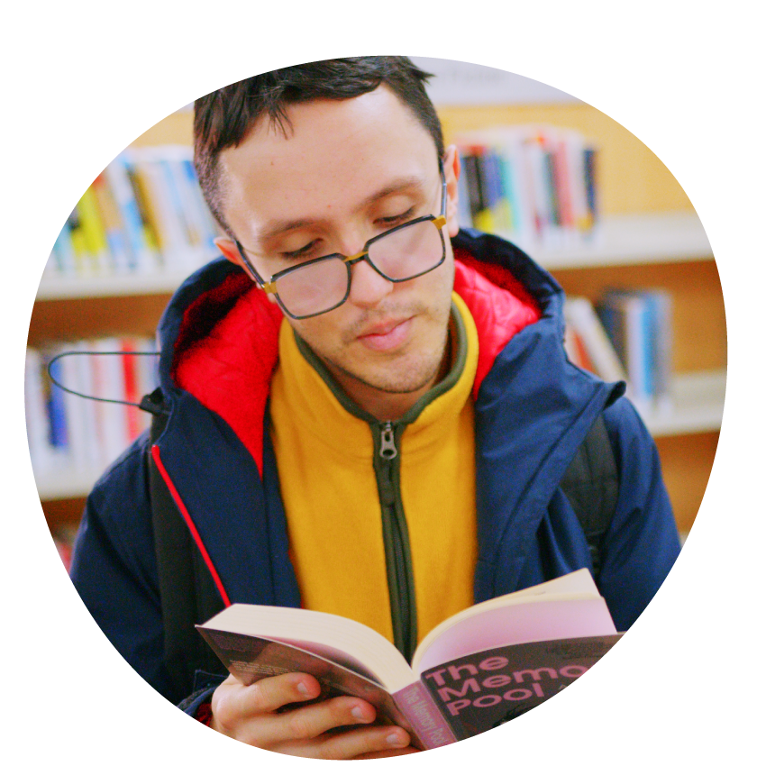 Image: A young adult in glasses reads a book in the library.