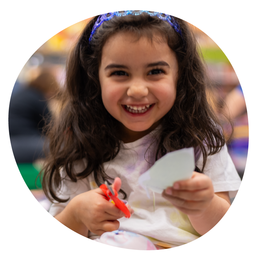 A smiling child sits cutting paper for a craft project