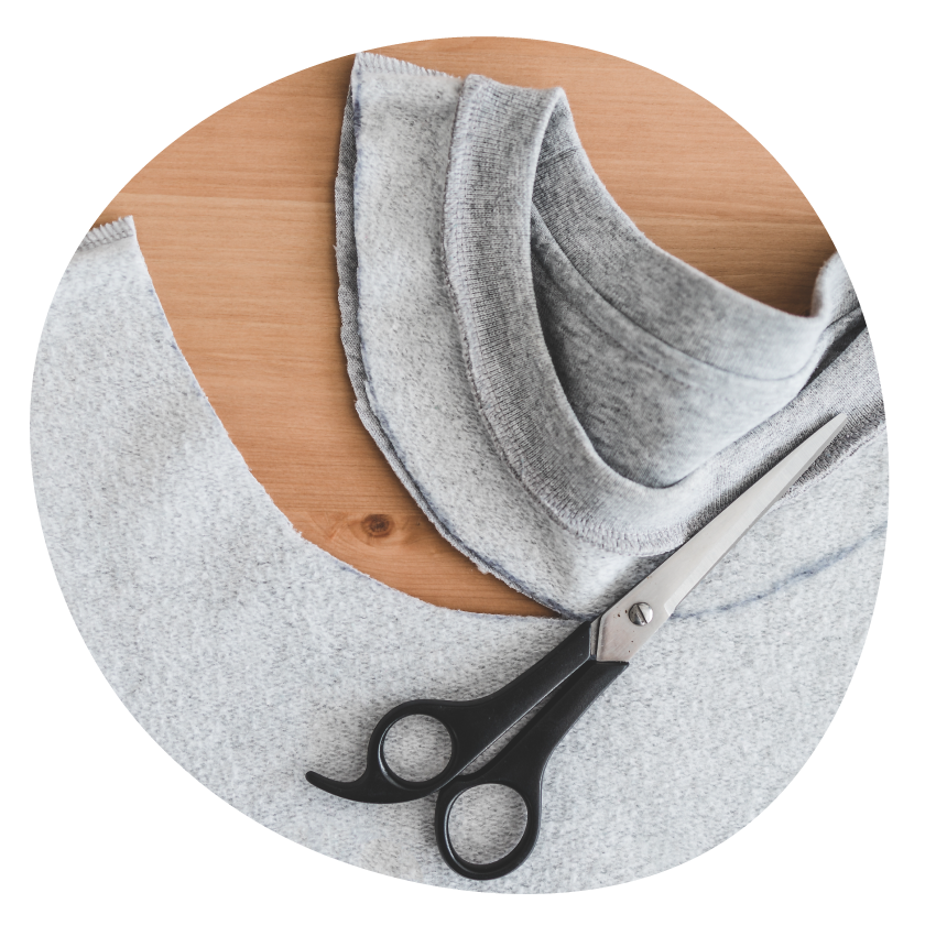 A grey T-shirt with the neckline partly cut away and a pair of scissors resting on top.