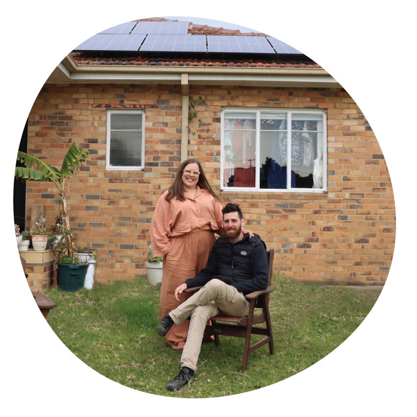 Email Image: A couple pose together in front of a brick house with solar panels on the roof.