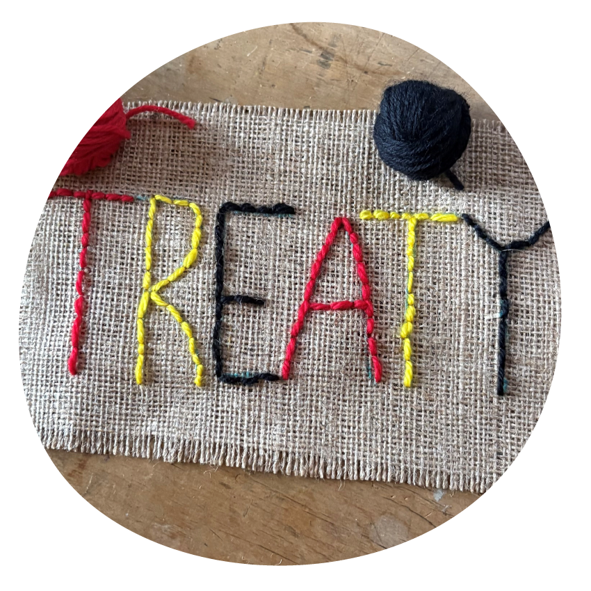 Cloth embroidered with the word TREATY in black, yellow and red, alongside three balls of wool in black, yellow and red.