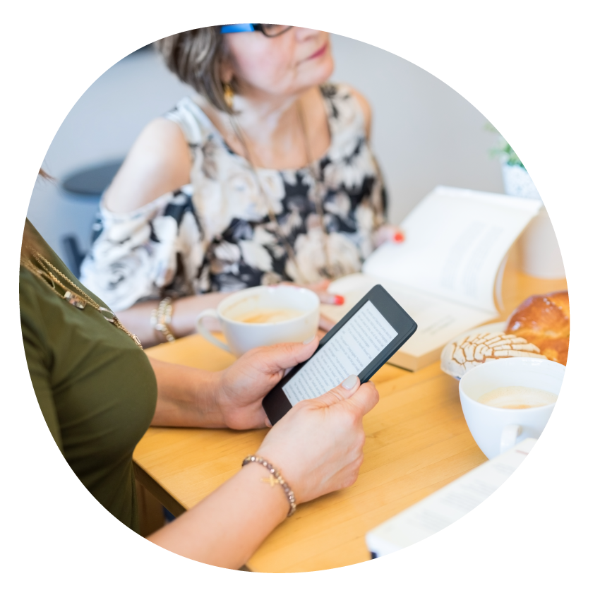 Image: People holding open books and an eReader seated around a table with coffee and snacks.