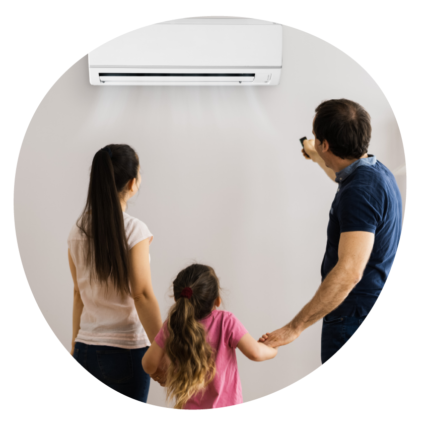 Image: Two adults and a child stand in a living room facing a wall-mounted air conditioner, one pointing a remote control