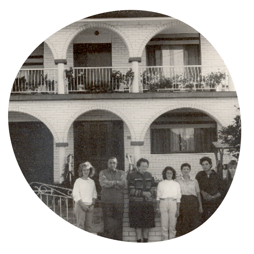 Email Image: Black and white photo of a group of people standing in front of a two-storey home with arches across the facade.