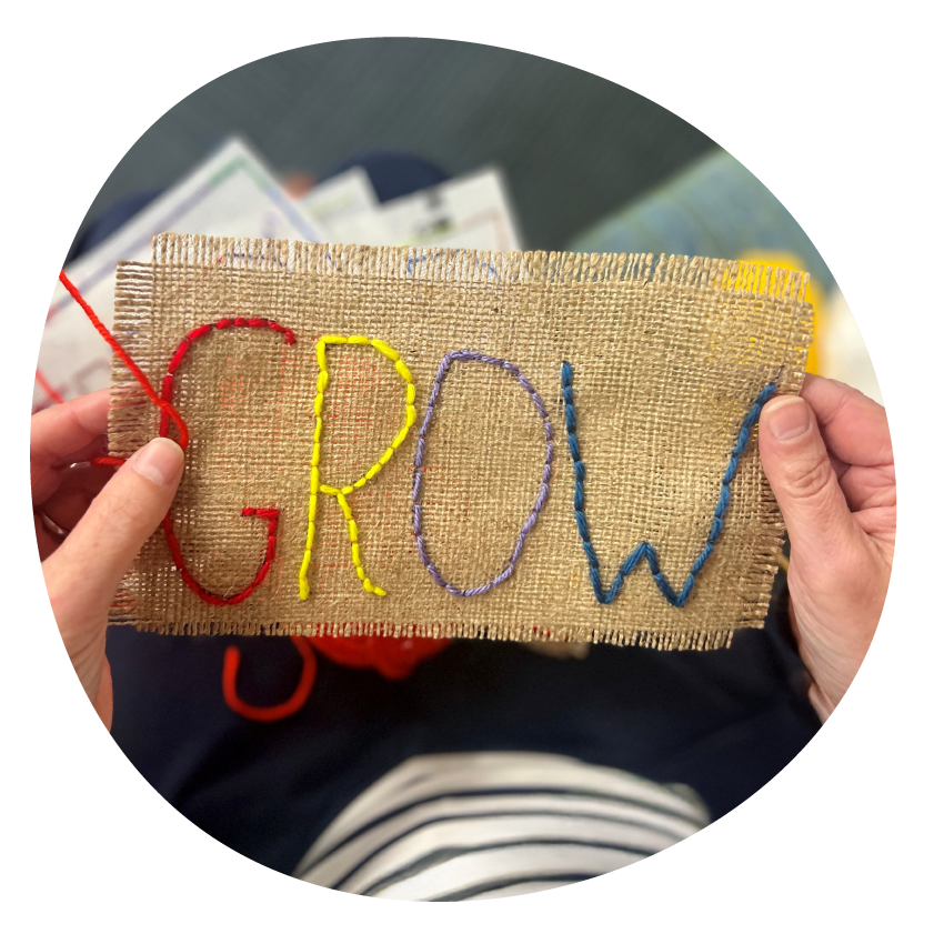 A hand holds a swatch of fabric embroidered with the word ‘grow’.