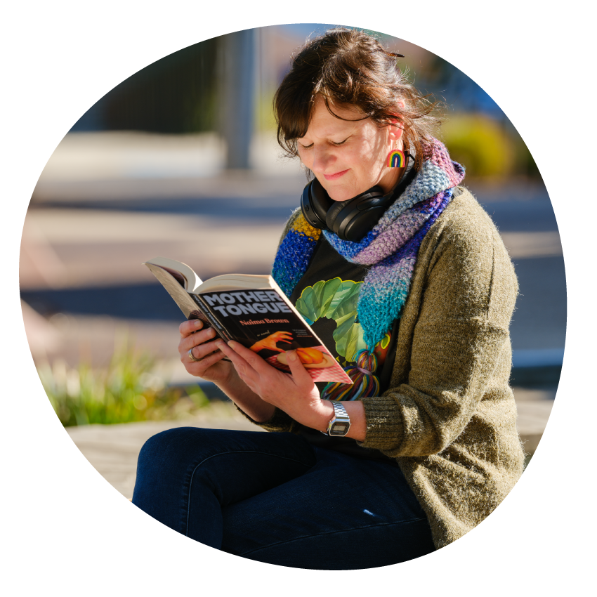 Email Image: A smiling woman seated outside on a sunny day reading a book.