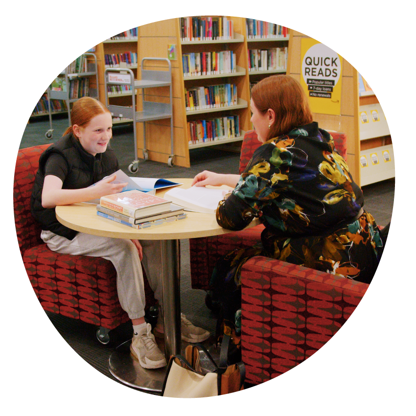 Email Image: An adult and child seated together at a library table covered with books
