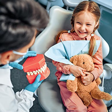 Child sitting in dental chair with stuffed bear in hand
