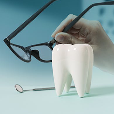 A dentist holding a pair of glasses with dental equipment near.