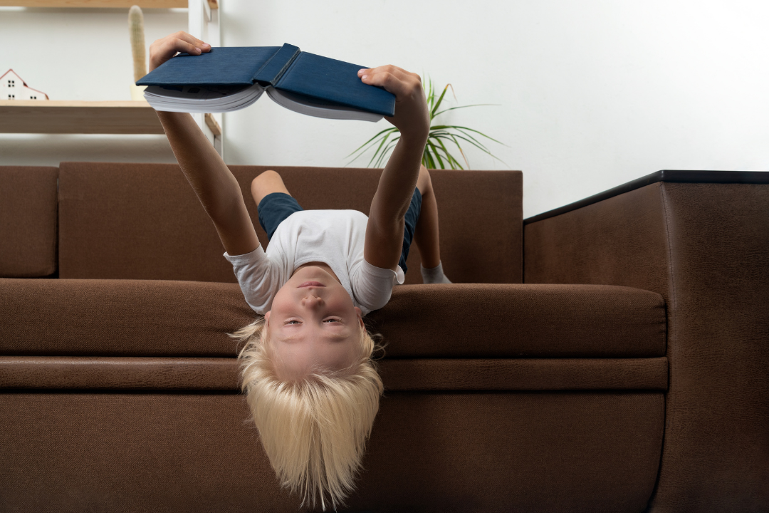 Child reading upside down hanging off a couch