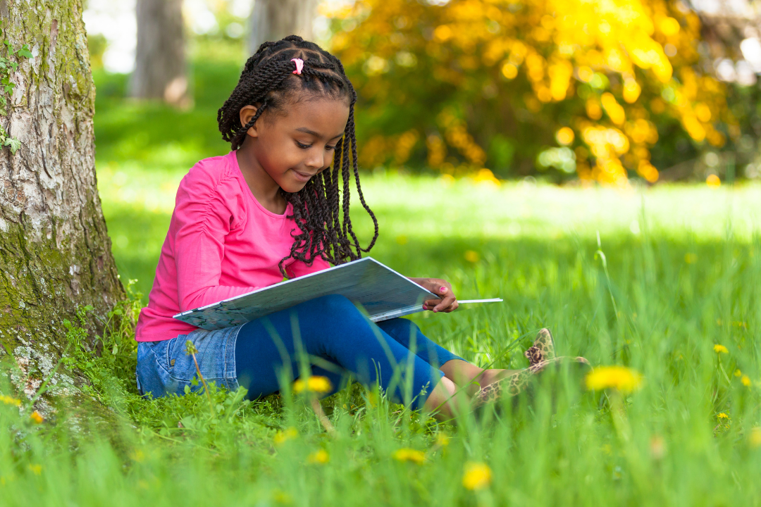 Child happily reading outside under a tree