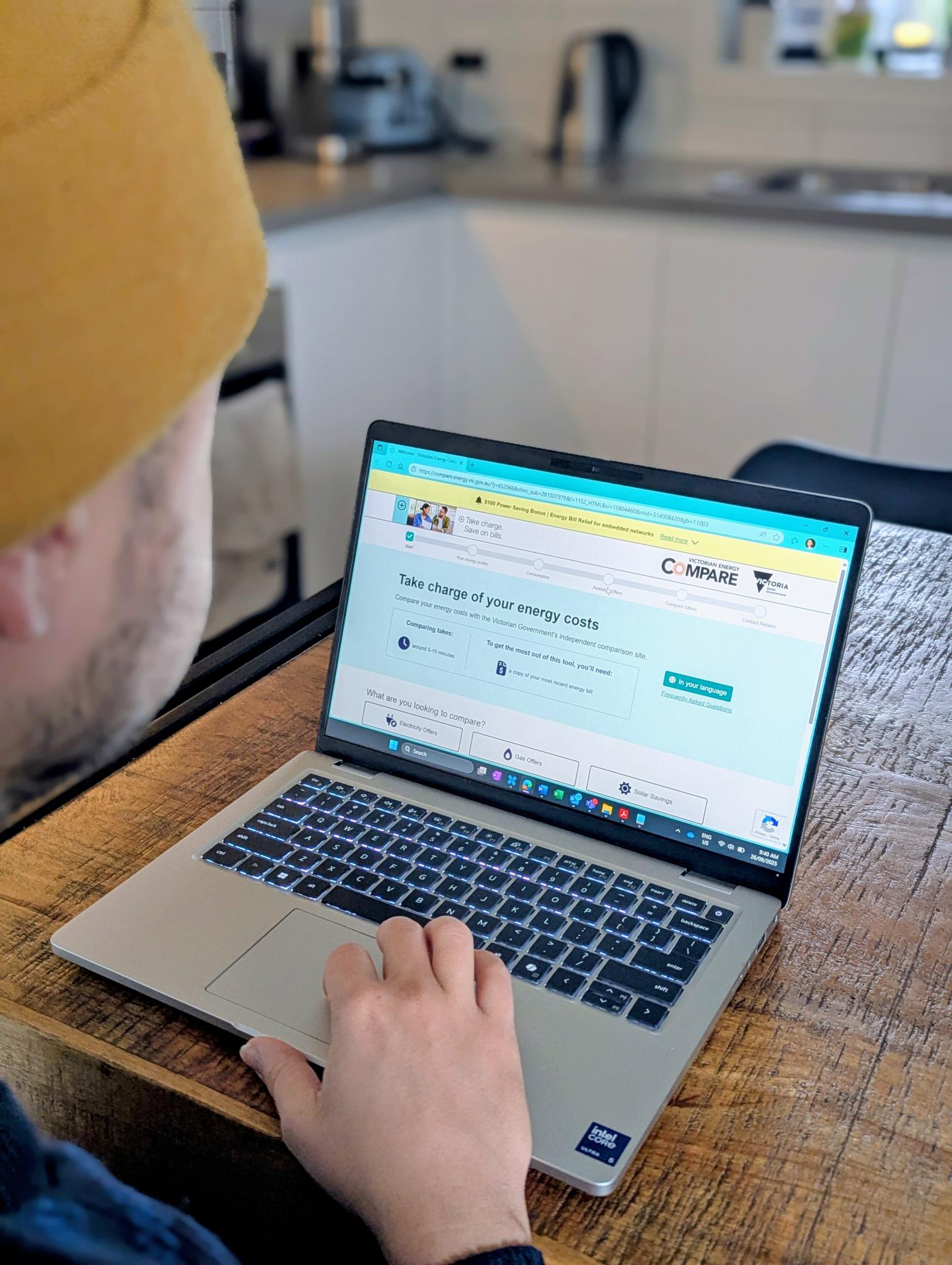 Person reading the Victorian Energy Compare website on their laptop while sitting in their kitchen