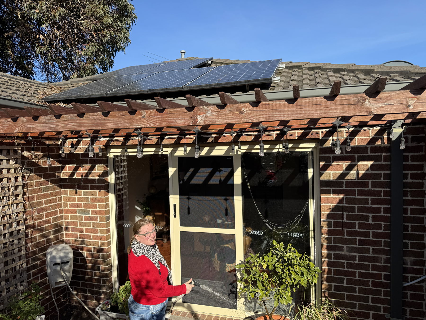 Emily watering her garden in her backyard with solar panels visible on the roof
