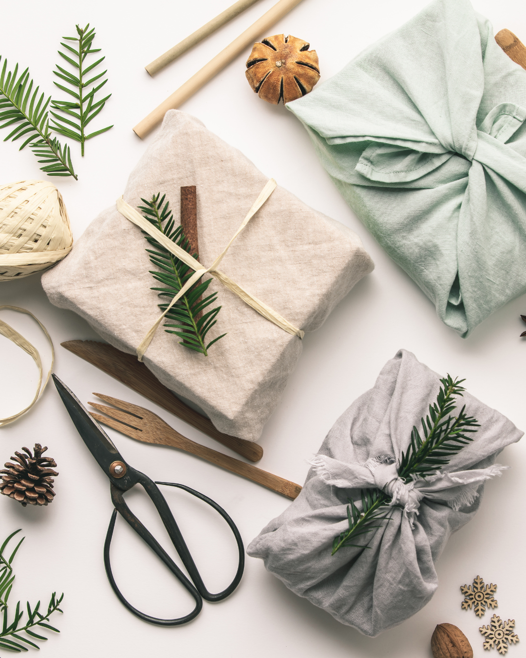Gifts wrapped in fabric with some decorative leaves and pine cones and a pair of scissors