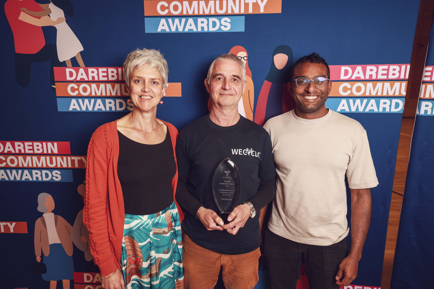 WeCycle team standing in front of Darebin Community Awards banner and holding their trophy
