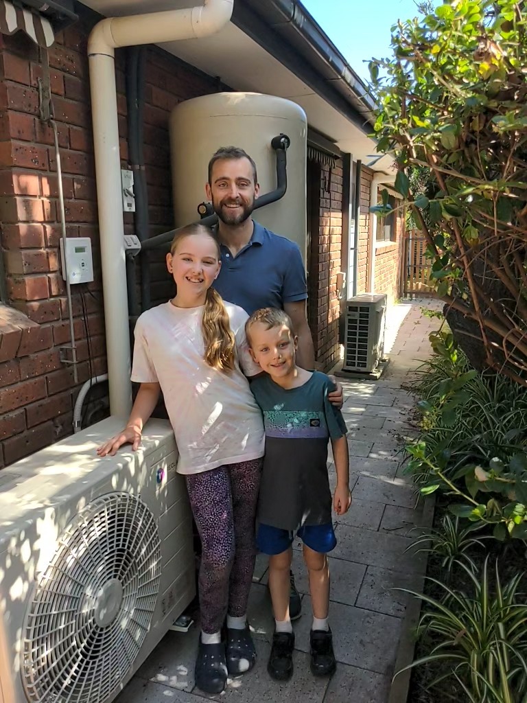Family standing in front of hot water heat pump in their backyard.