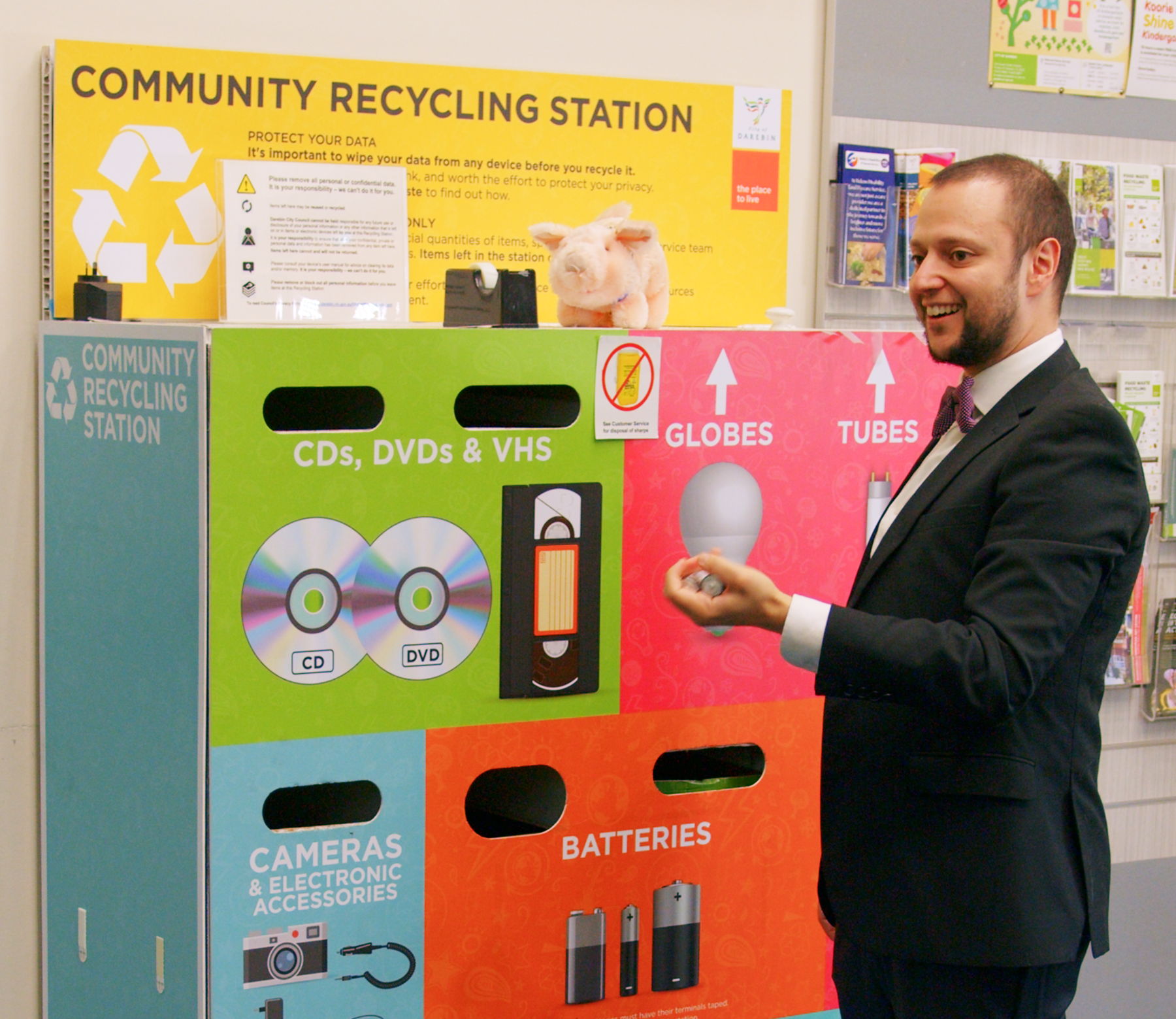 Man wearing a suit and bow tie standing in front of a community recycling station at Preston Customer Service Centre holding batteries in his hands
