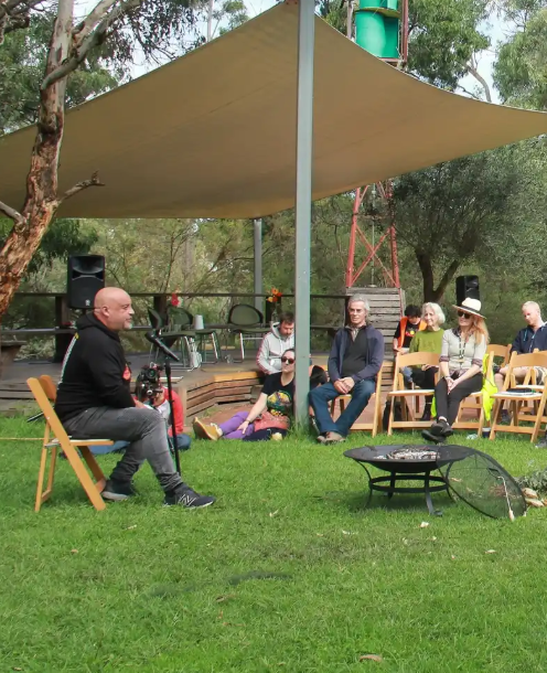 people sitting on chairs listening to Wurrundjeri Woi Wurrung Elder, Uncle Bill Nicholson speak into a microphone