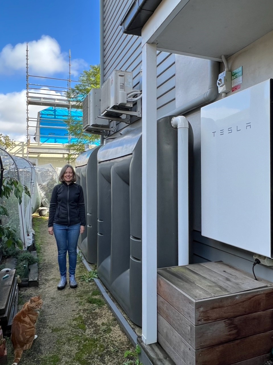 Person standing in their backayrd near a garden, water tank and solar battery.