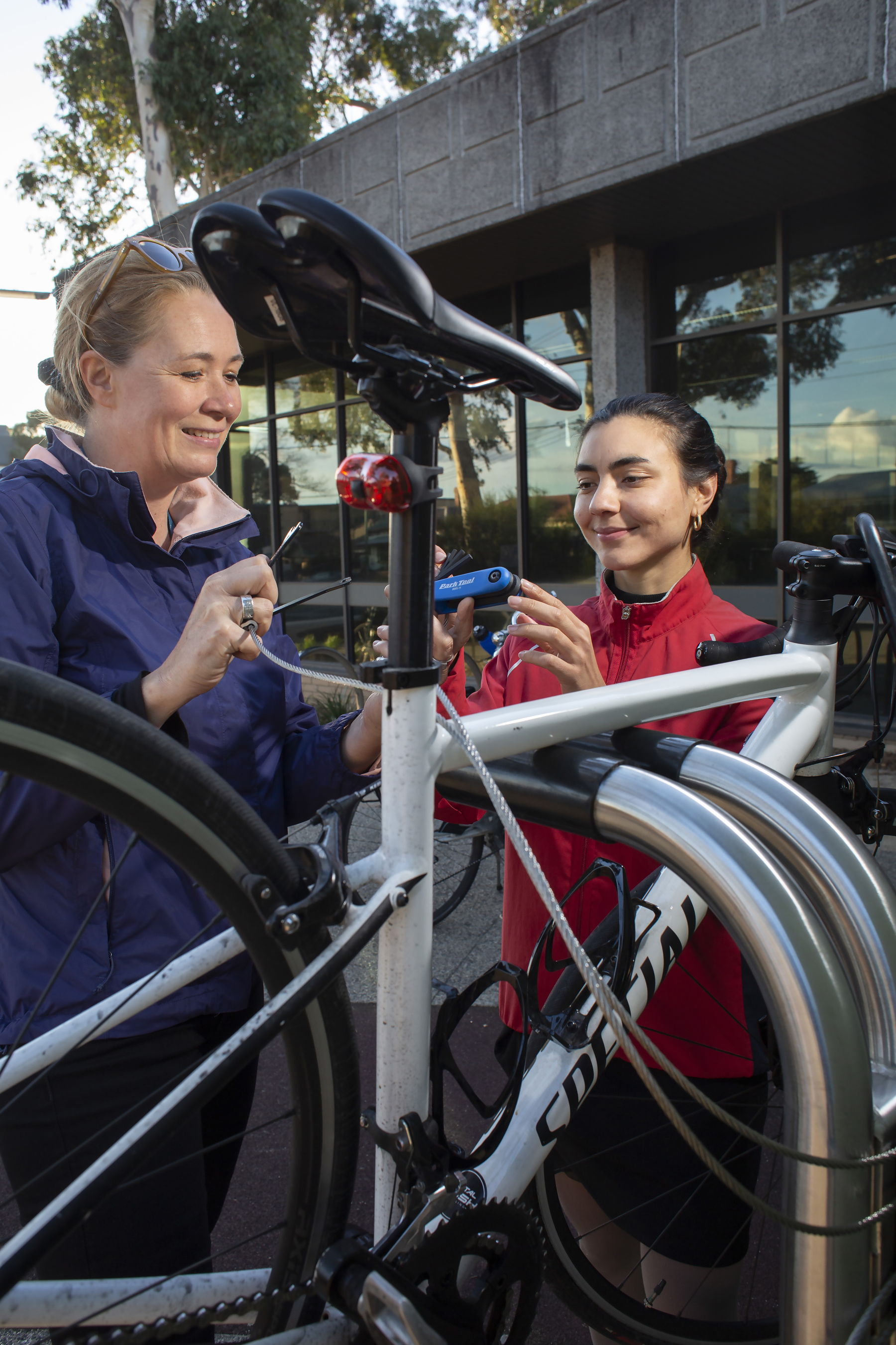 Two women holding tools and smiling while their bicycle is on a stand.