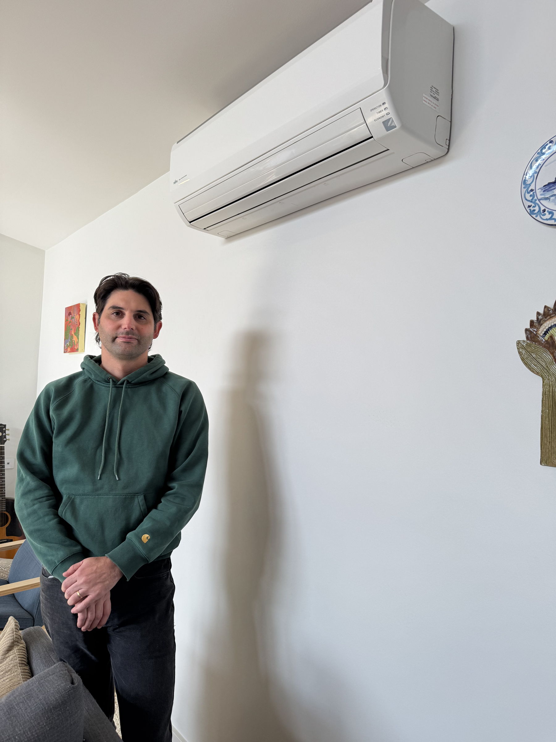 Person in a green hoodie standing next to a wall mounted split system 