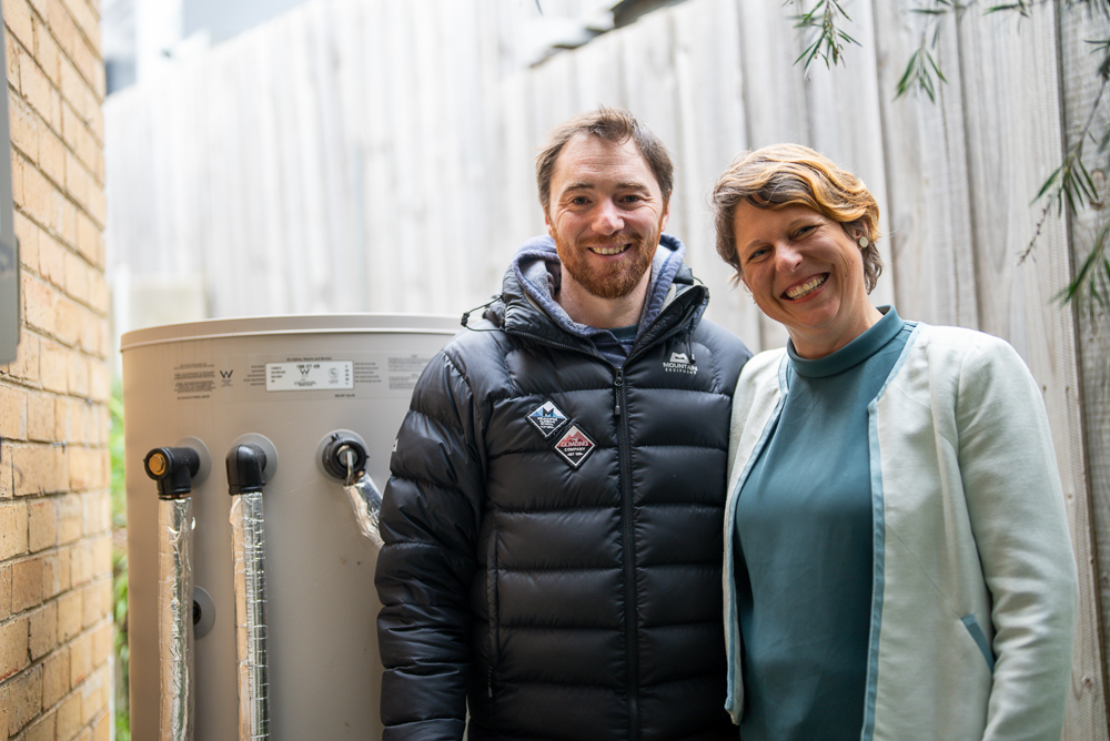 Two smiling people standing next to their heat pump hot water system.